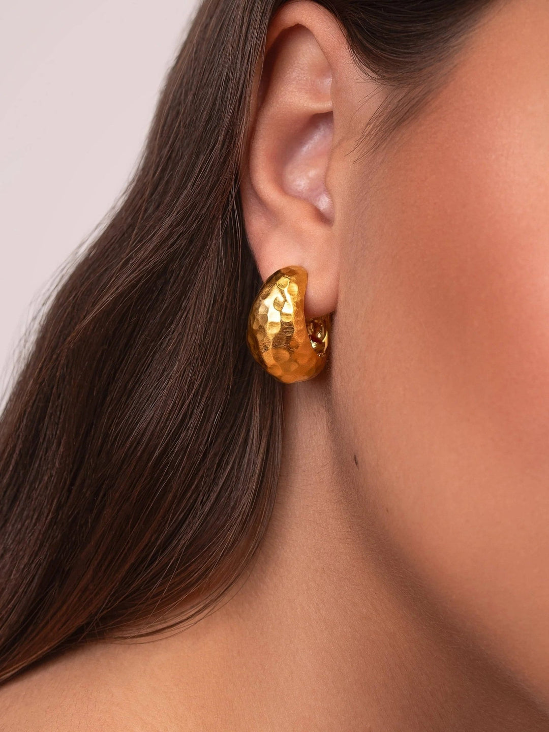 Woman wearing gold hammered hoop earrings, side profile