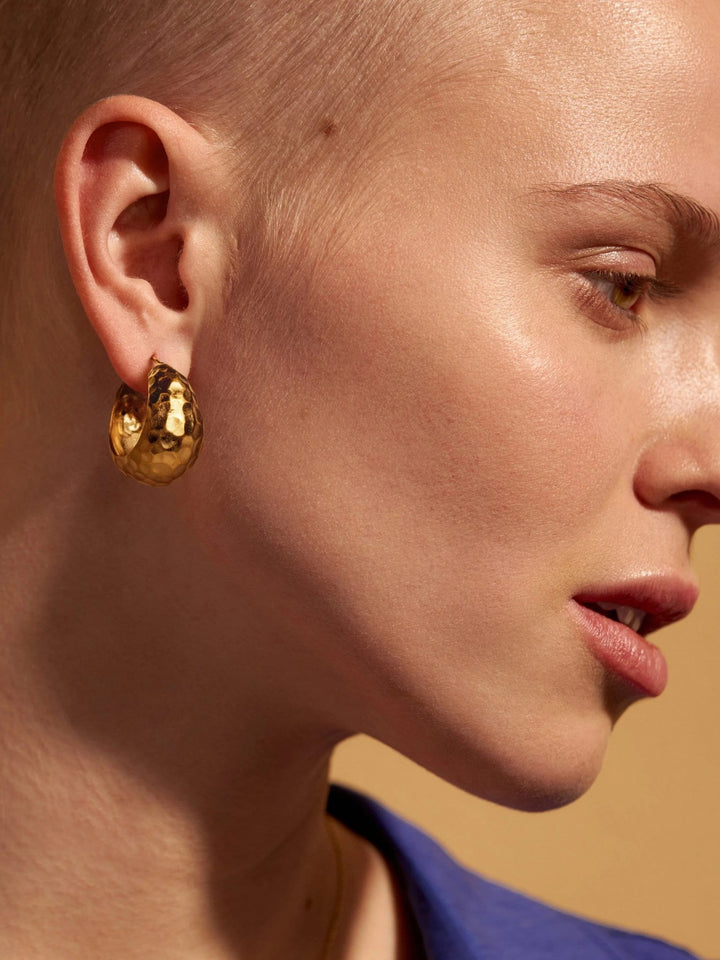 Model with short hair wearing gold textured hoop earrings