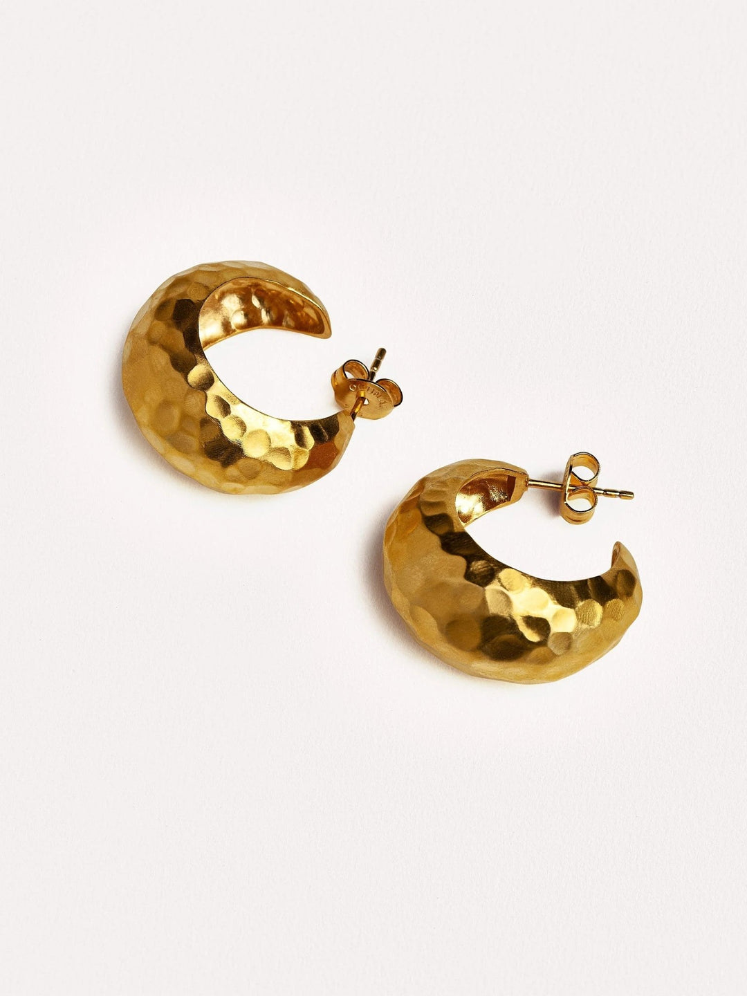 Gold textured hoop earrings displayed on a neutral surface