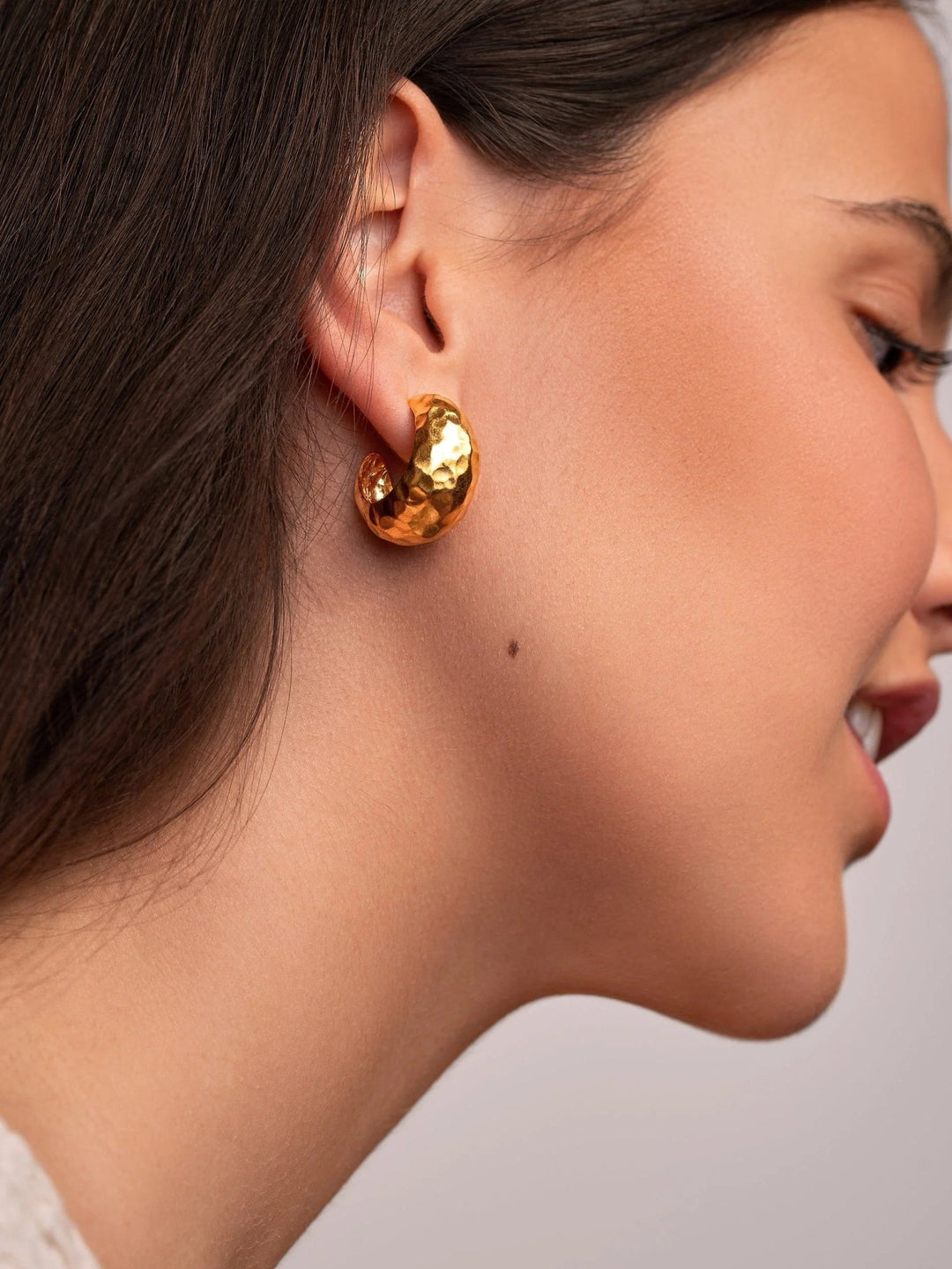 Woman wearing 24K gold-plated hammered hoop earrings, side profile