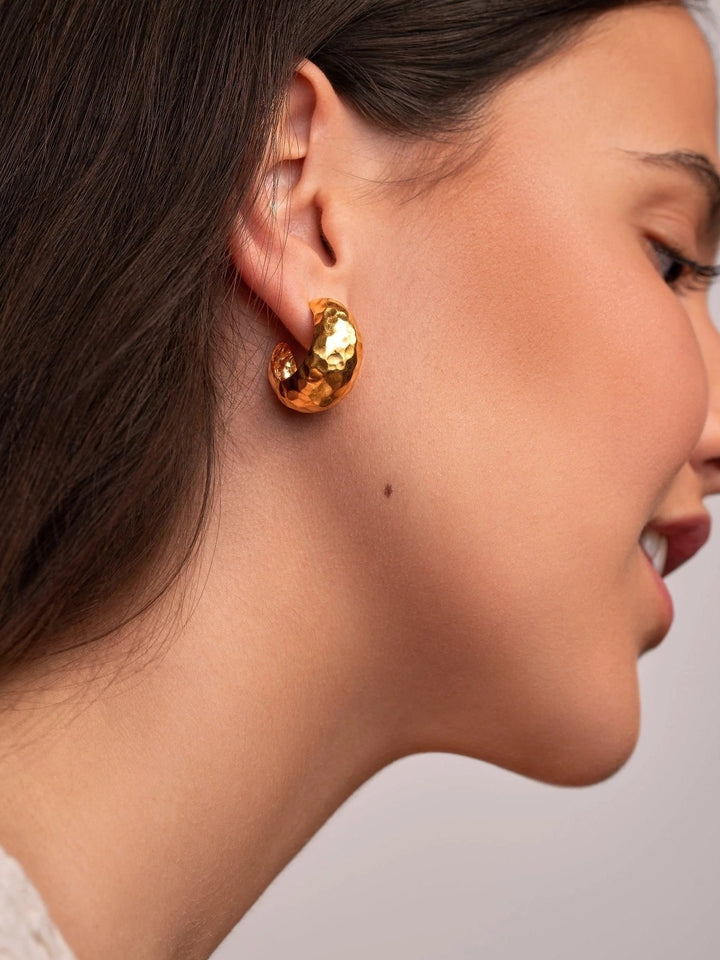 Woman wearing 24K gold-plated hammered hoop earrings, side profile