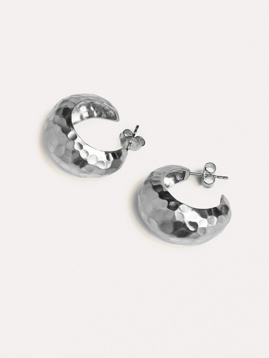 Close-up of silver hammered hoop earrings displayed on neutral background