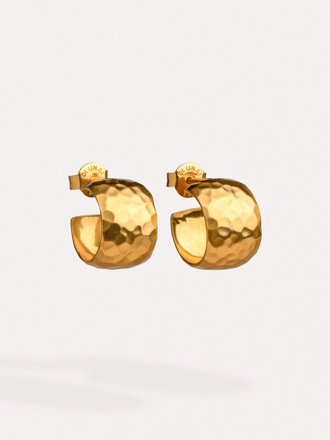 Chunky gold hoop earrings in 24K gold-plated brass, resting on soft fabric.