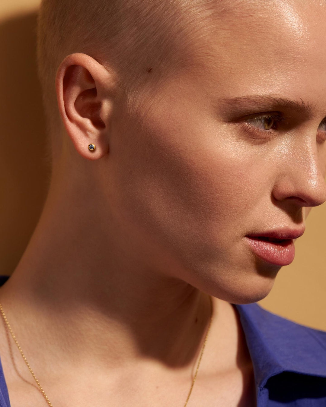 Model with a shaved head wearing a gold earring against a warm-toned background.