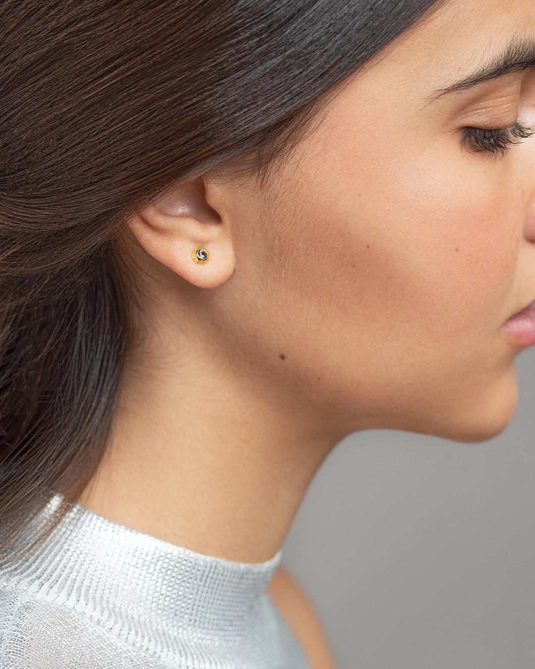 Profile view of a woman wearing a small gold stud earring against a neutral background.