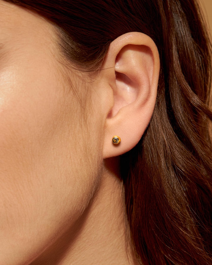 Minimalist gold earring with a dark stone on a woman with long hair.