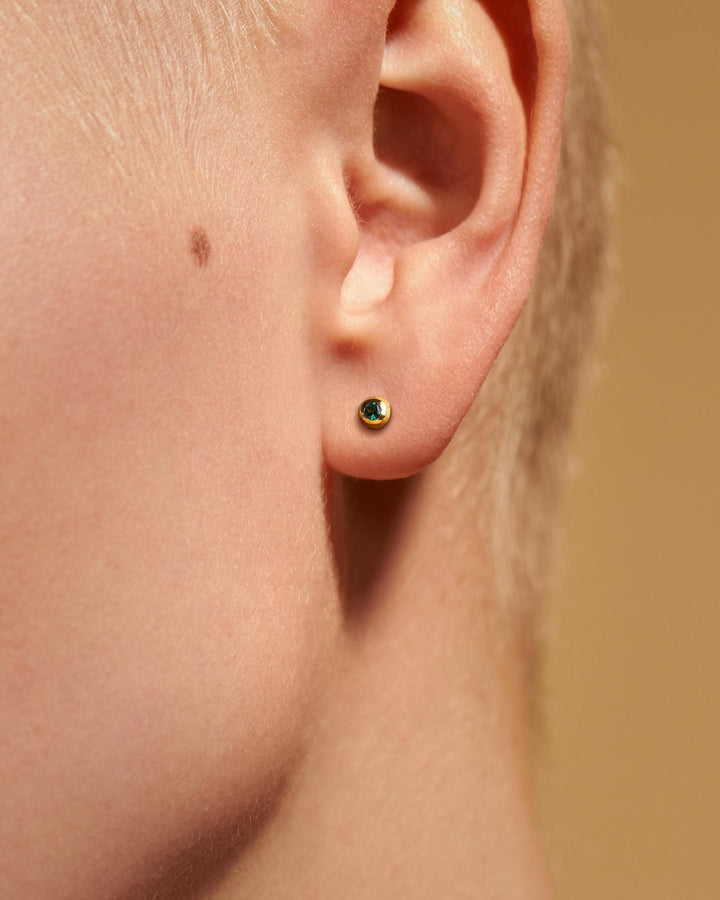 Gold stud earring with a green stone on a fair-skinned woman with short hair.