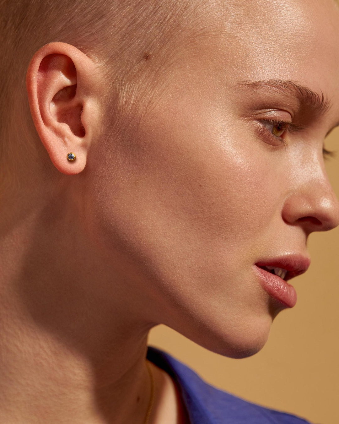 Profile portrait of a model with a shaved head wearing a gold earring with a dark stone.