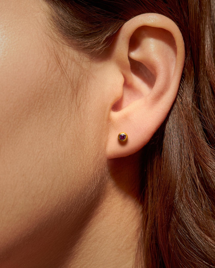 Close-up of a gold stud earring with a aquamarine stone on a woman's ear.studsLunai Jewelry