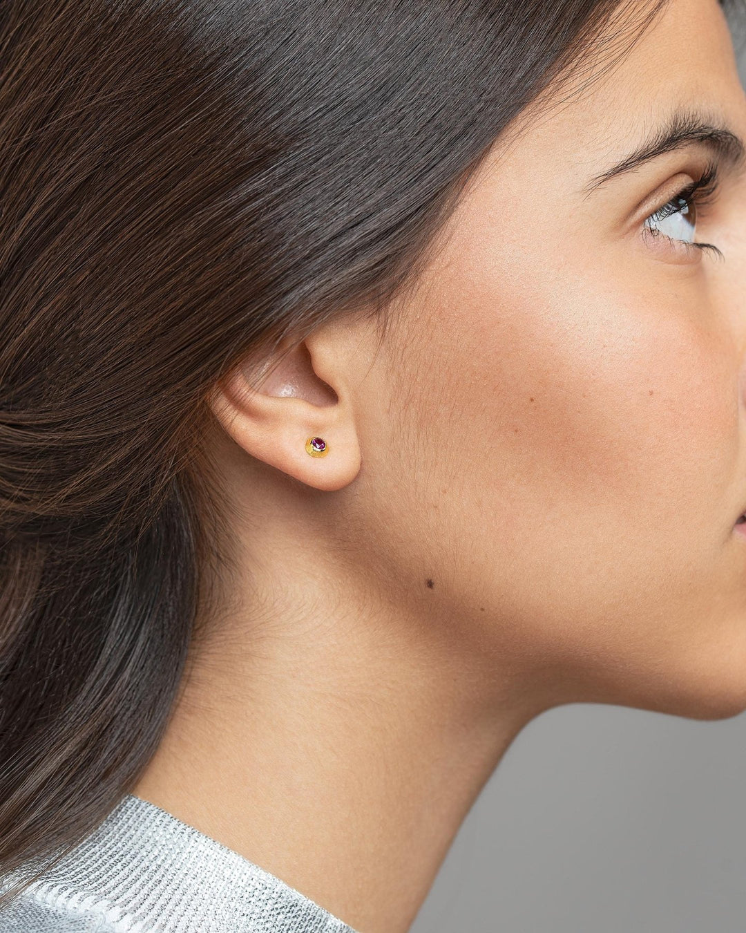 Side view of a woman with tied-back hair wearing a minimalist gold earring.