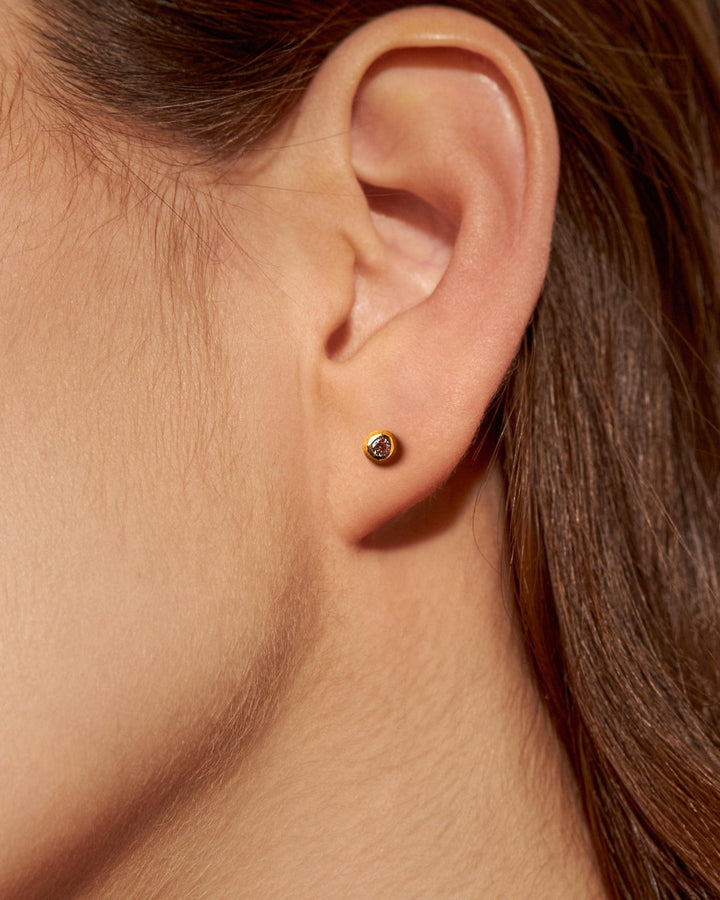 Gold stud earring with a small stone on a fair-skinned woman with tied-back hair.