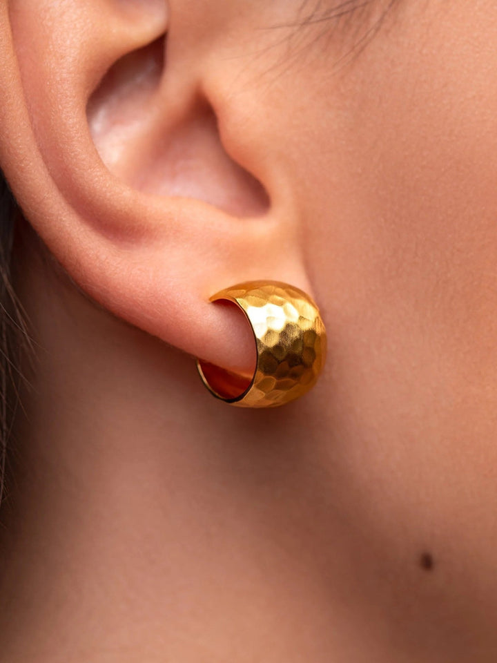 Close-up of a woman wearing gold hammered huggie hoops.