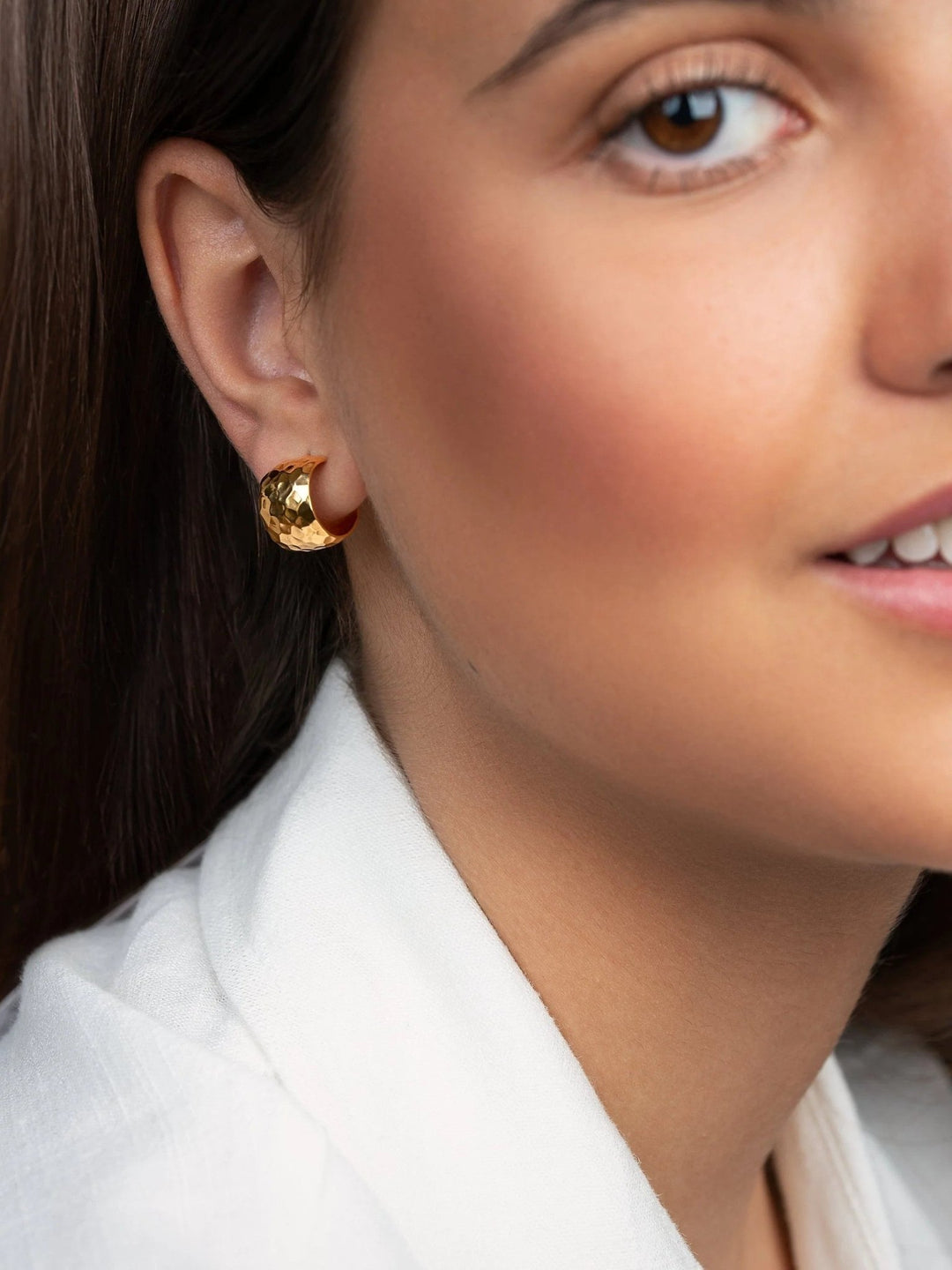 Close-up of a woman wearing gold hammered huggie hoops, smiling.