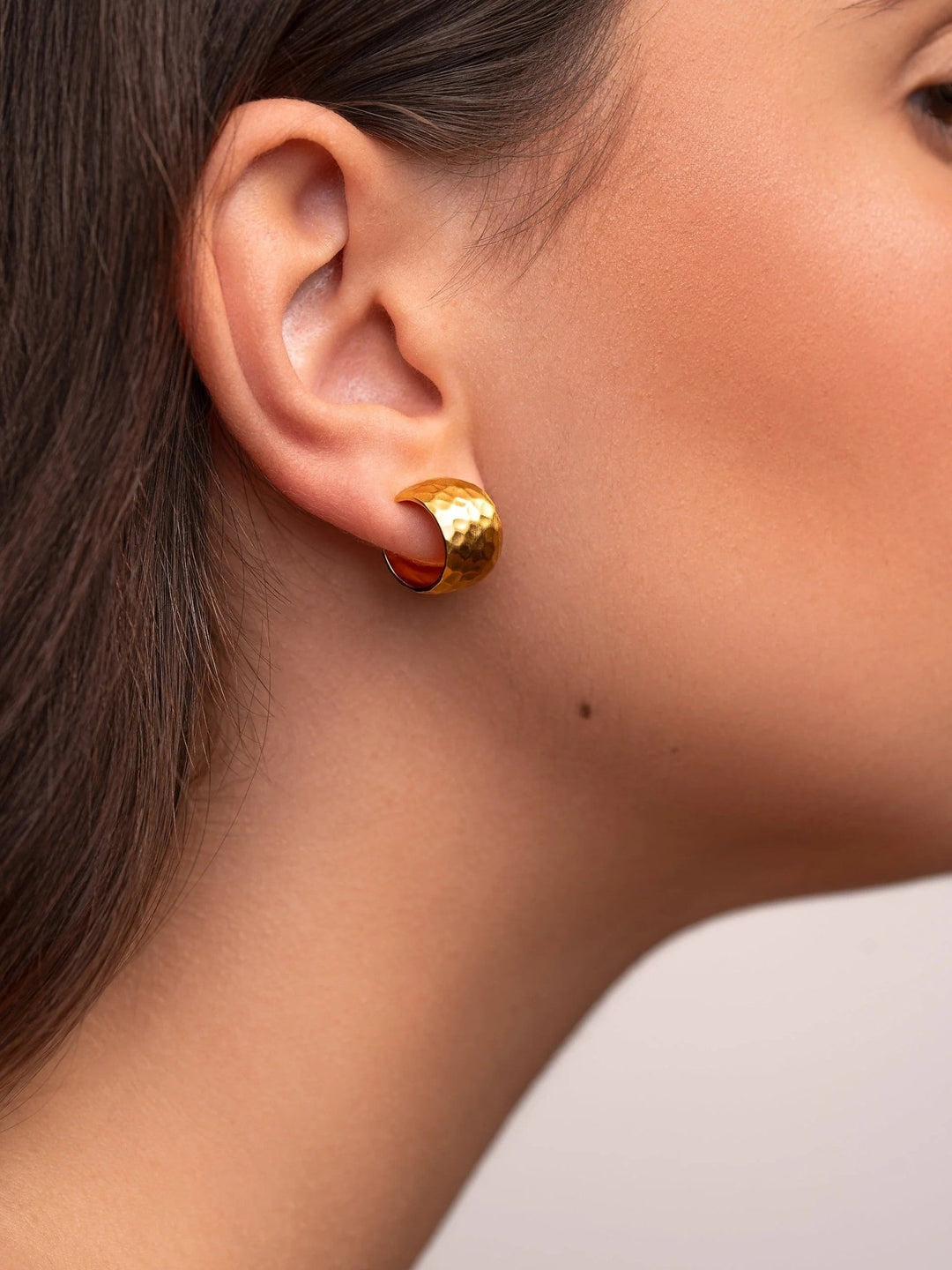 Side view of a woman wearing gold hammered huggie hoops.