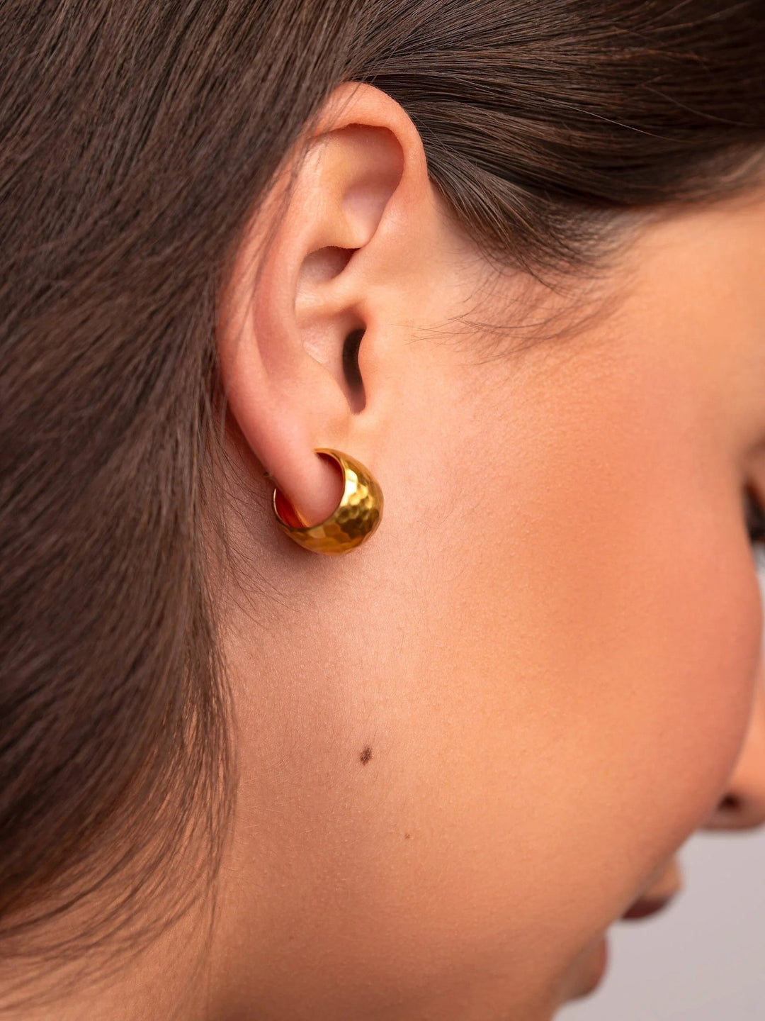 Side angle of a woman wearing gold hammered huggie hoops.